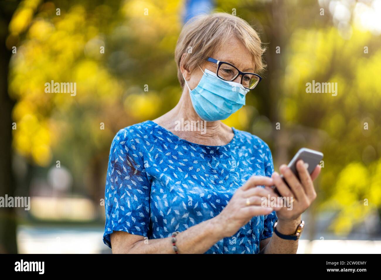 Senior woman using smartphone while wearing protective face mask Stock Photo