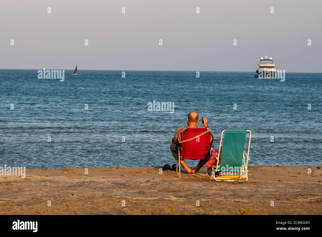 Unrecognised man sitting on a sandy beach enjoying the sea at sunset. Stock Photo