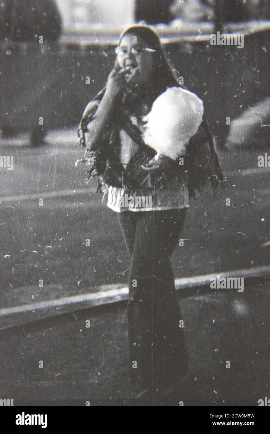 Fine 1970s vintage black and white photography of a cute girl eating a fluff of cotton candy at the evening street fair carnival. Stock Photo