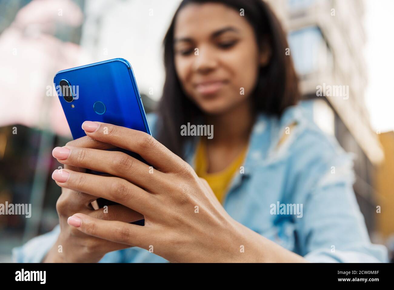 Young smiling casual african woman using mobile phone on a street, close up Stock Photo