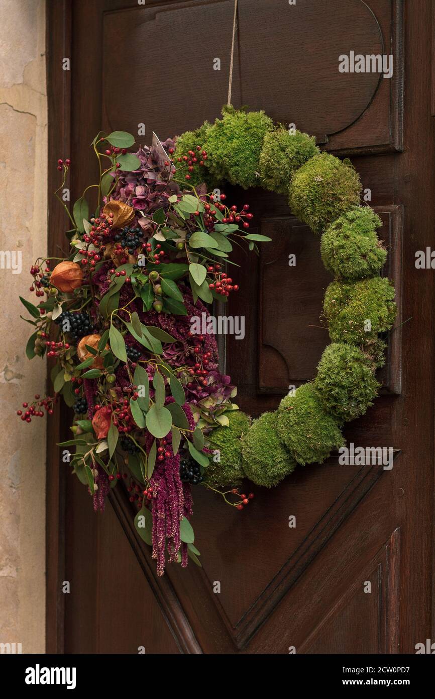 Wreath with the red berries and the dry leaves and fruits hanging on a door. Stock Photo