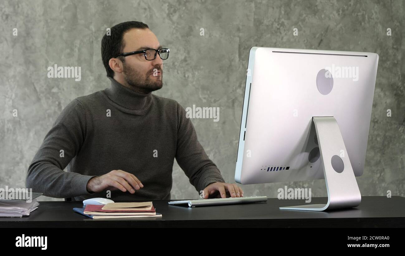 Angry man sitting at the table with computer over gray backgroun Stock Photo