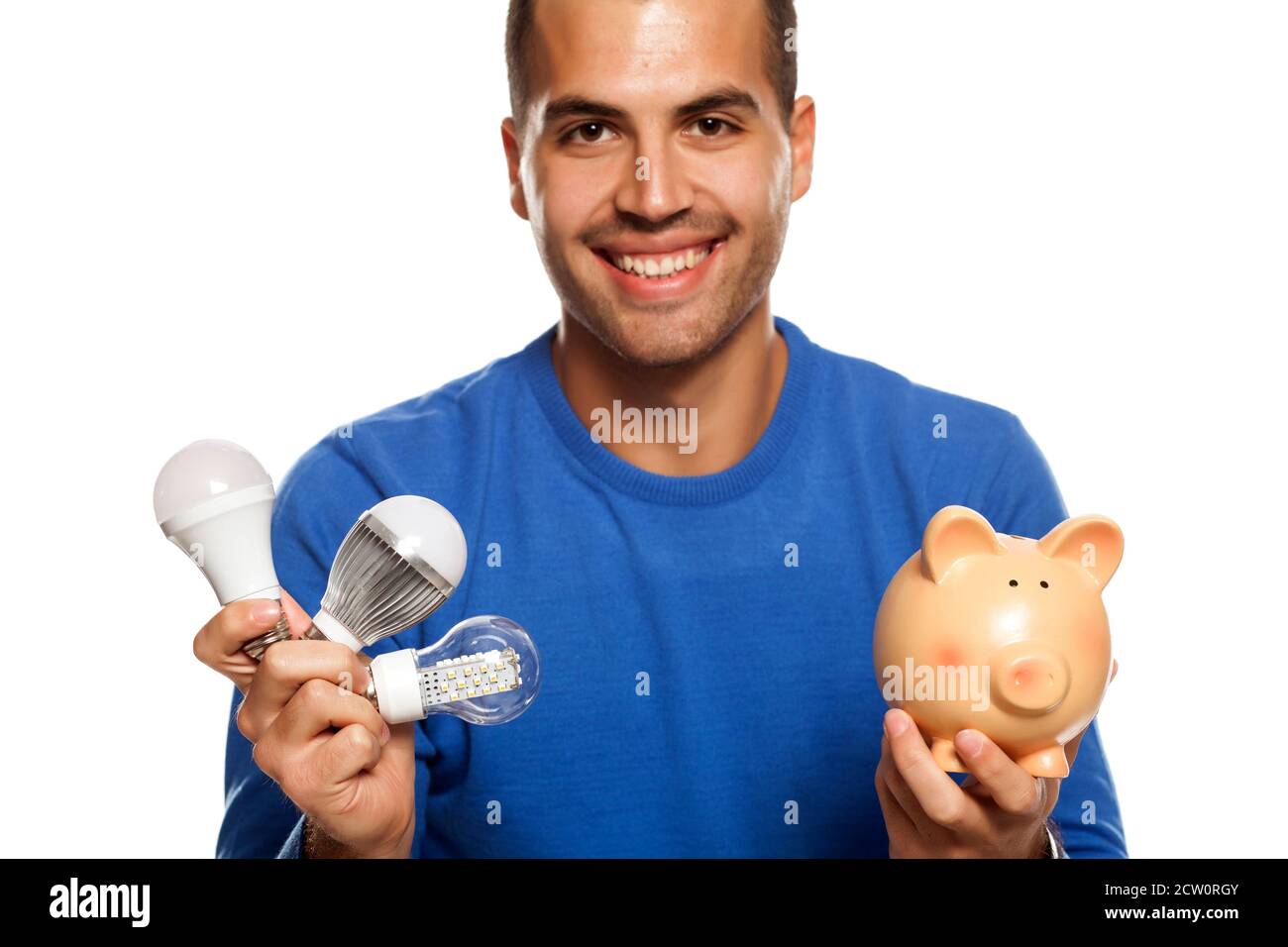 portrait of happy young man, holding three different LED bulbs and piggy bank on white background Stock Photo