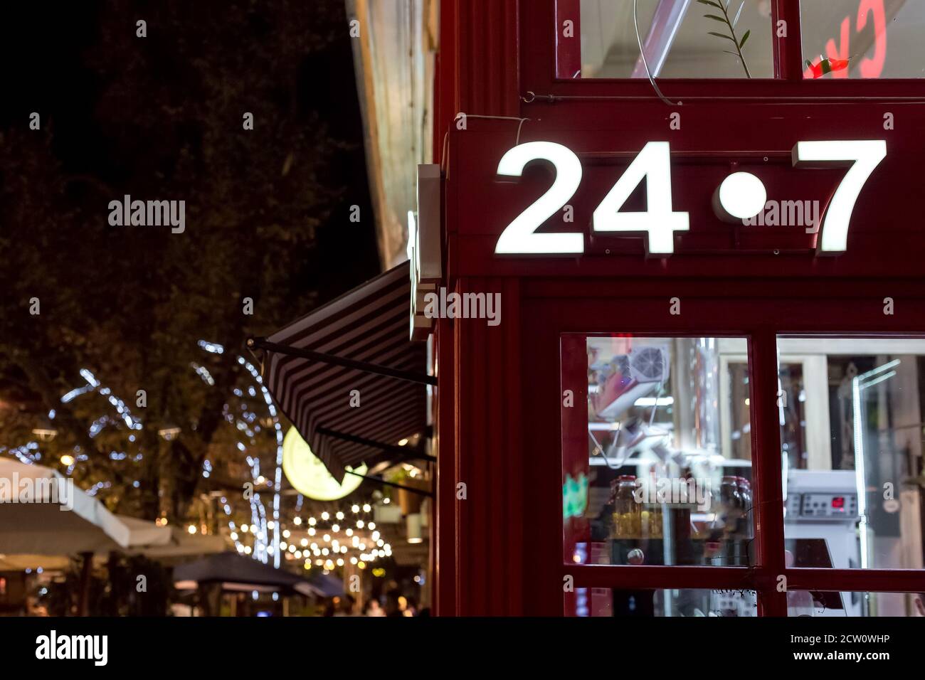 facade of red shop on corner with luminous signboard 24/7 round the