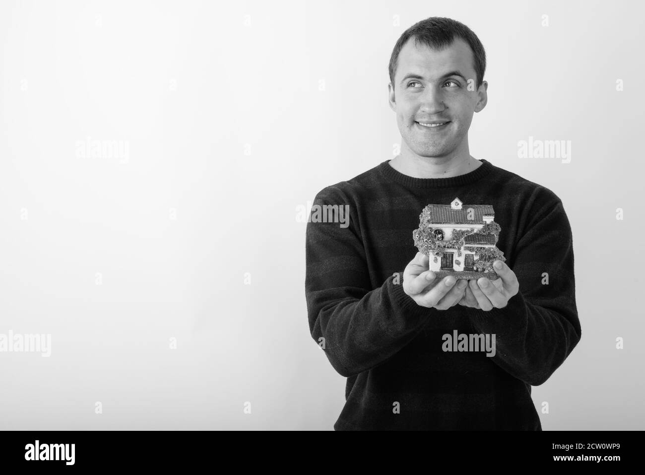Studio shot of young happy muscular man smiling and thinking while holding house figurine against white background Stock Photo