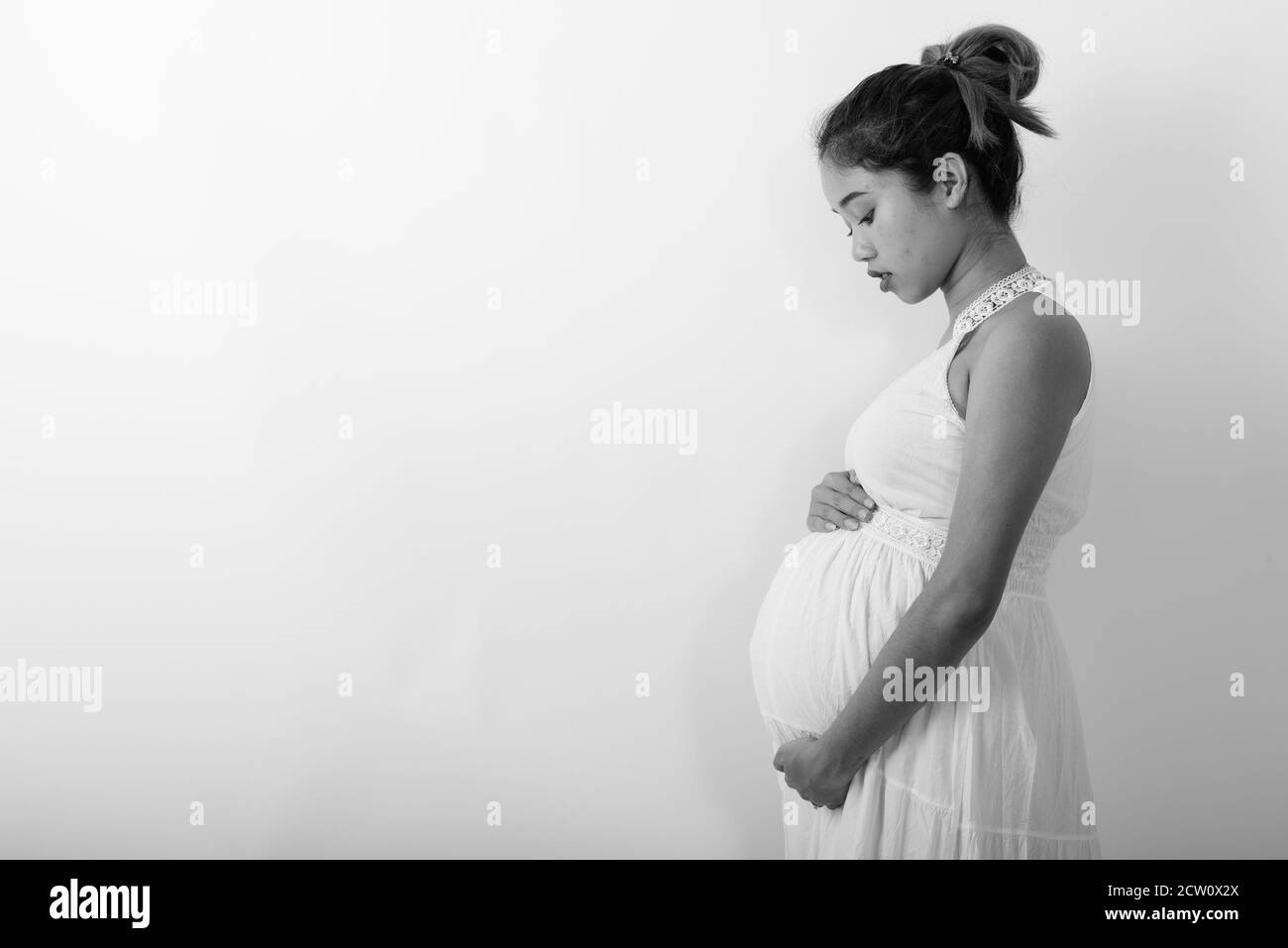 Profile view of young Asian pregnant woman holding her stomach against white background Stock Photo
