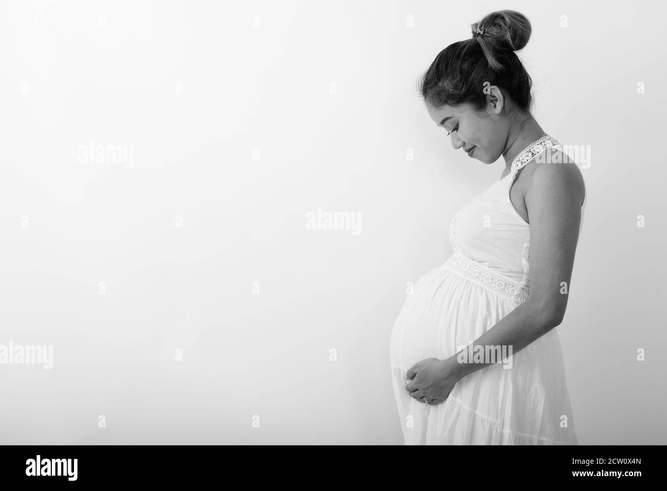 Profile view of young Asian pregnant woman holding while looking at her stomach against white background Stock Photo