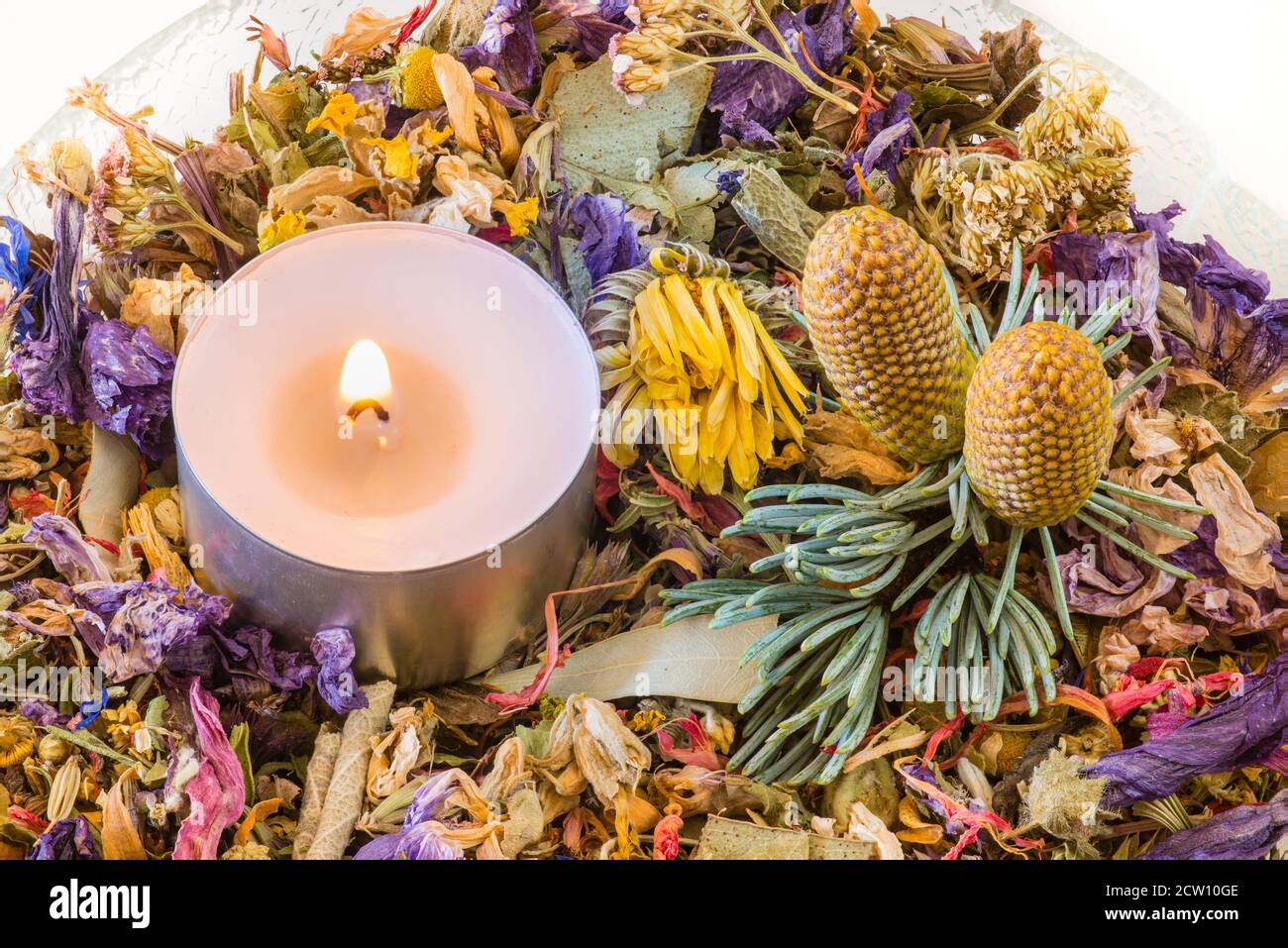 Glass bowl with potpourri of dried flowers, candle and two pinecones