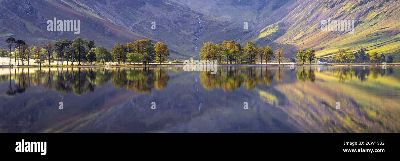 The famous Char Hut and Sentinel Trees at Buttermere are reflected in the calm waters as the morning light highlights the surrounding fells. Stock Photo