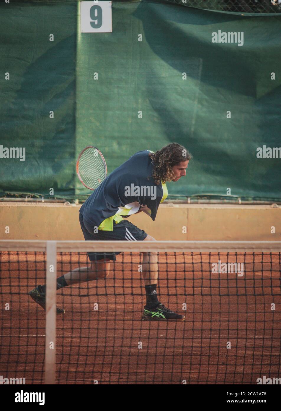 Split Croatia September 2020 Man with long hair in sports shirt and pants playing tennis, swining an underhand ball. Vertical shot, seen from the dist Stock Photo