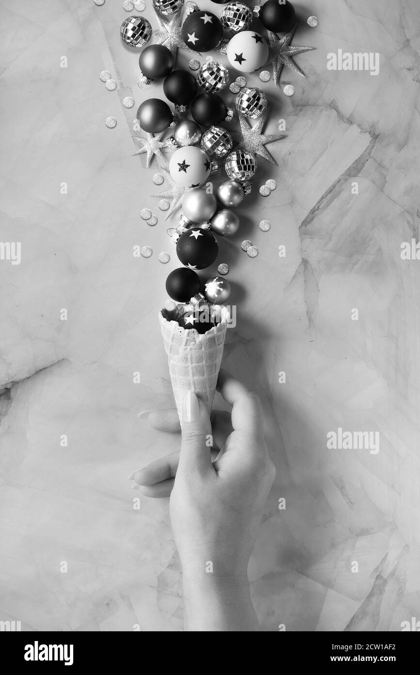 Creative Christmas or New Year flat lay. Hand with ice cream waffle cone with Xmas decorations. Stock Photo