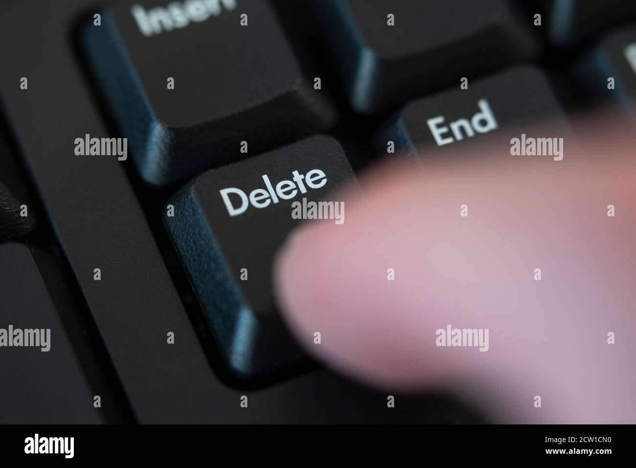 A macro closeup of a finger pushing the delete button on a computer keyboard. Concept: delete, remove, cancel, erase, cancel culture, deleted Stock Photo