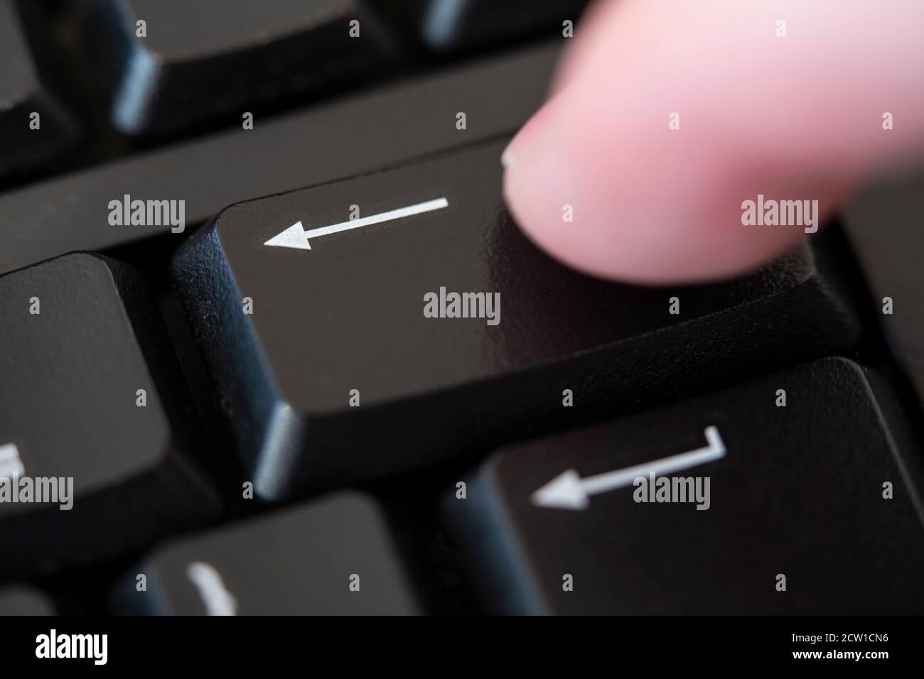 A macro closeup of a finger pushing the backspace key on a computer keyboard. Concept: delete, remove, cancel, erase, cancel culture, deleted Stock Photo