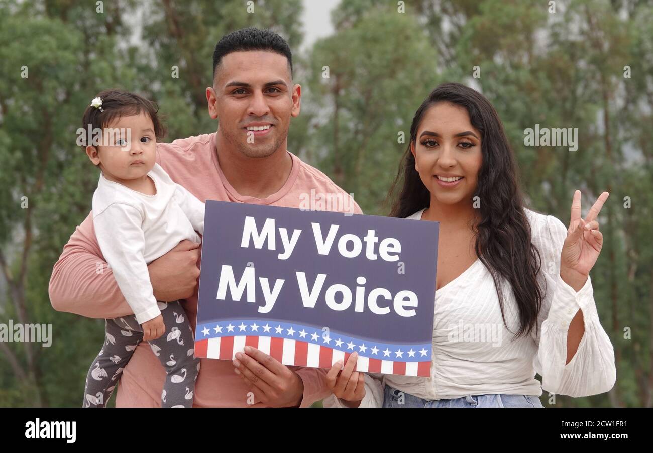 A young Latino family holds up a voting sign and smiles for the camera Stock Photo