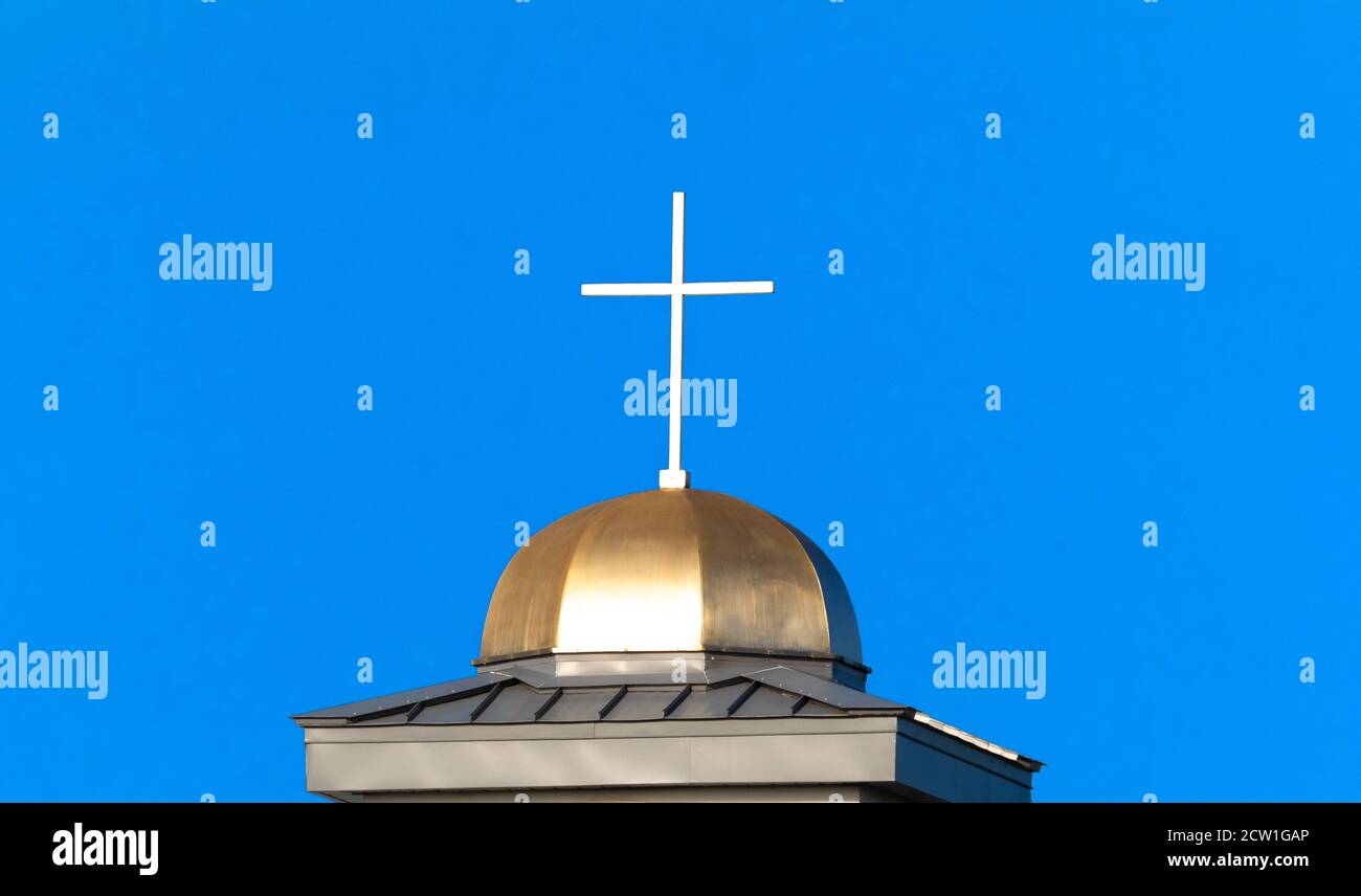 White cross aganist a blue sky on top of gold dome of Catholic church Stock Photo