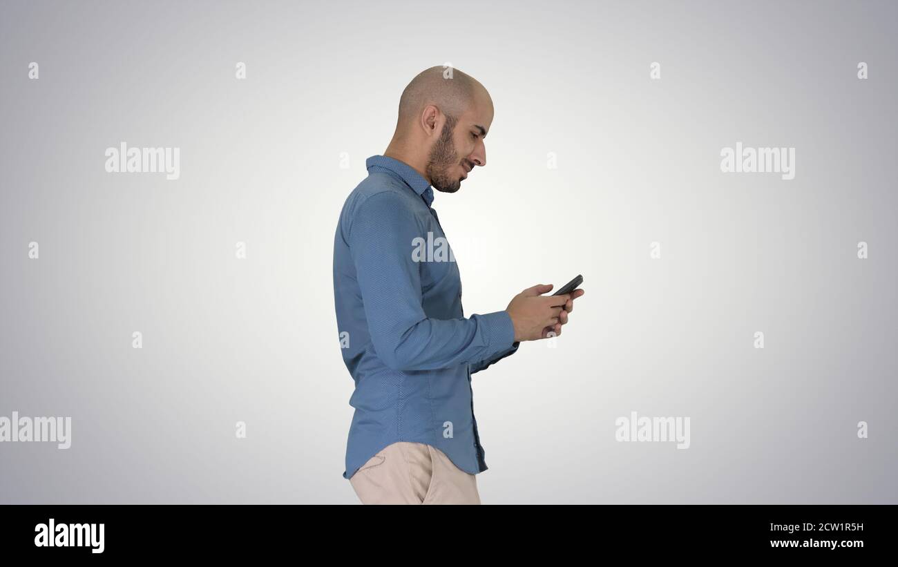 Young man walking and using a phone on gradient background. Stock Photo