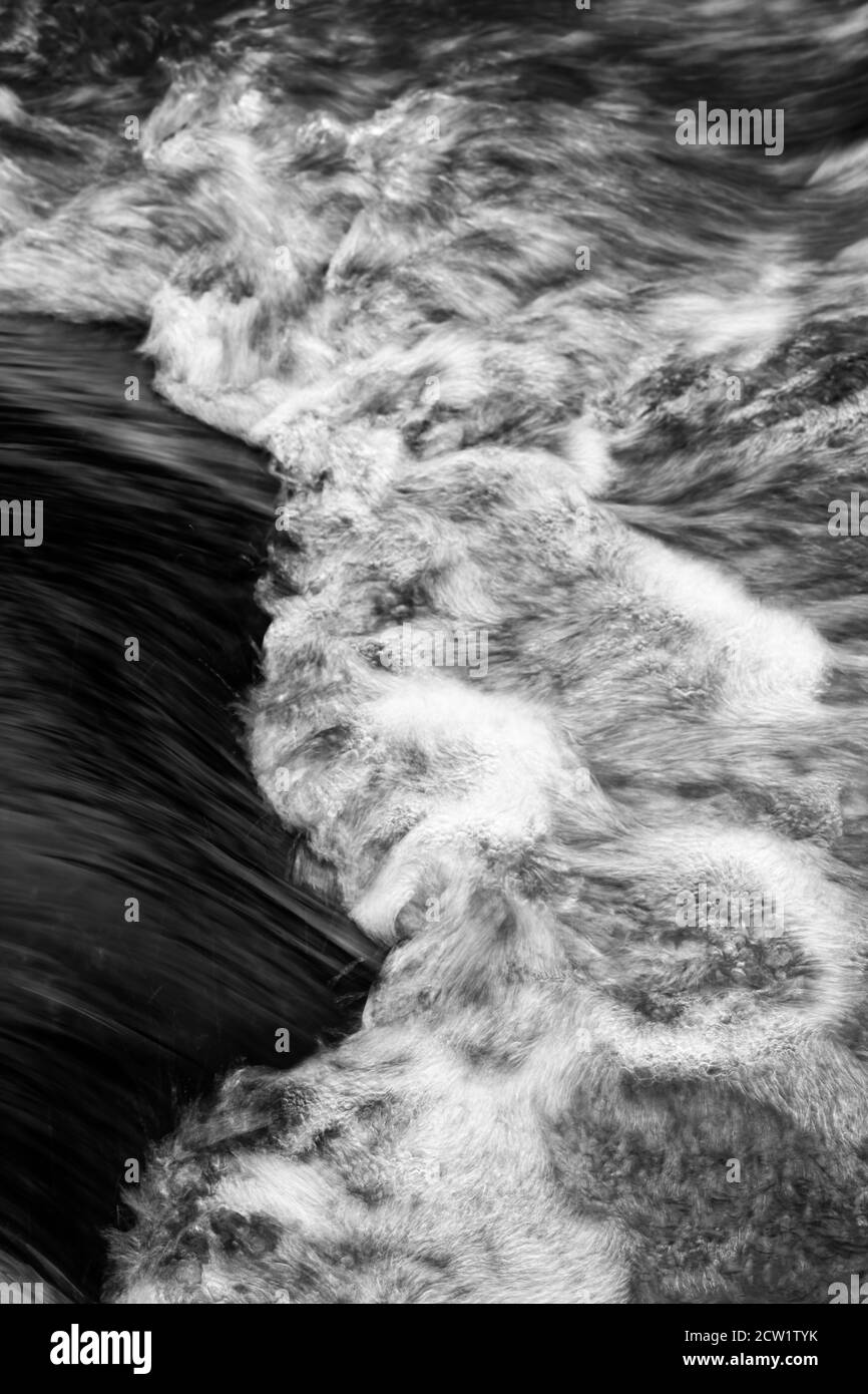 Detail view of flowing water of a small river, high-contrast black and white image, flowing structure, long time exposure, narrow focus zone Stock Photo