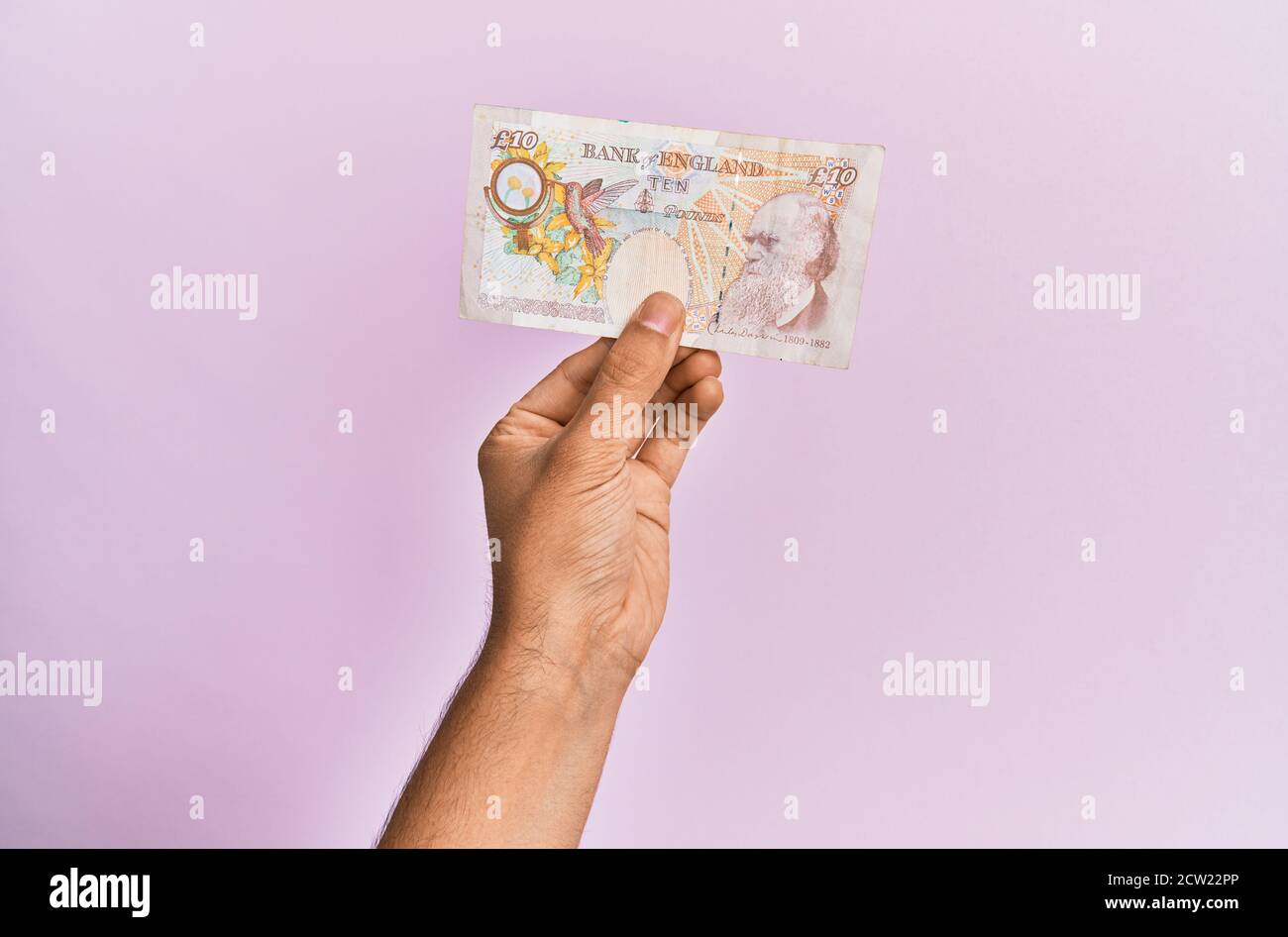 Hispanic hand holding one uk 10 pounds banknote over isolated pink ...