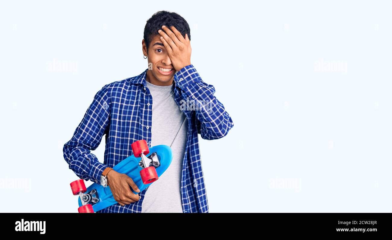 Young african amercian man holding skate stressed and frustrated with hand on head, surprised and angry face Stock Photo