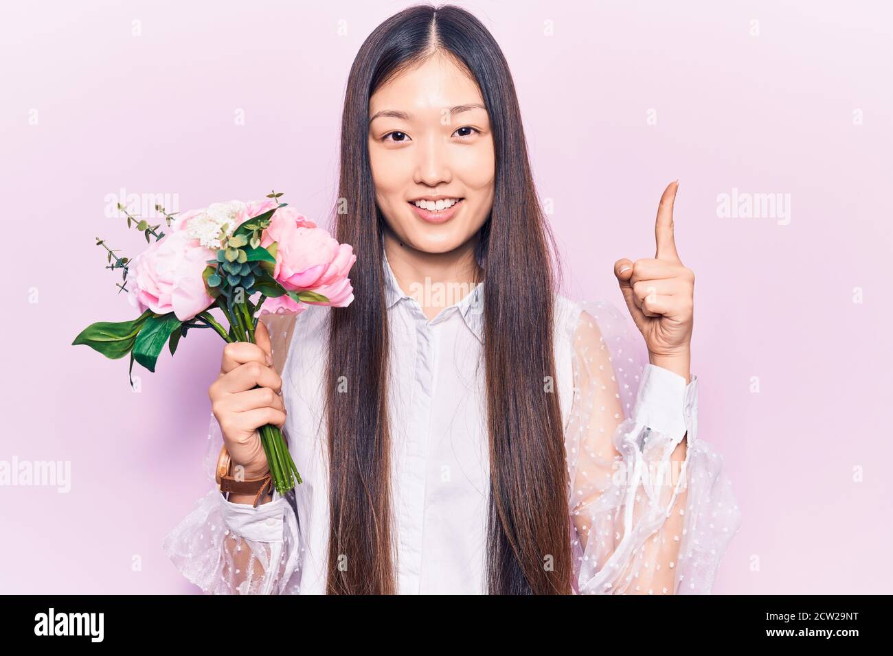 Young beautiful chinese woman holding pink bouquet of flowers smiling ...
