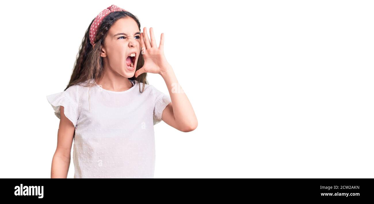 Cute hispanic child girl wearing casual white tshirt shouting and screaming loud to side with hand on mouth. communication concept. Stock Photo