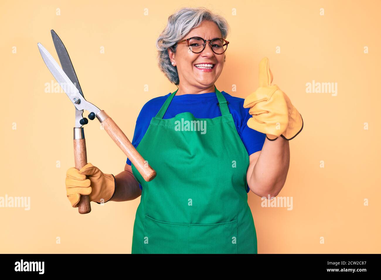 Senior hispanic woman wearing gardener apron and gloves holding shears ...