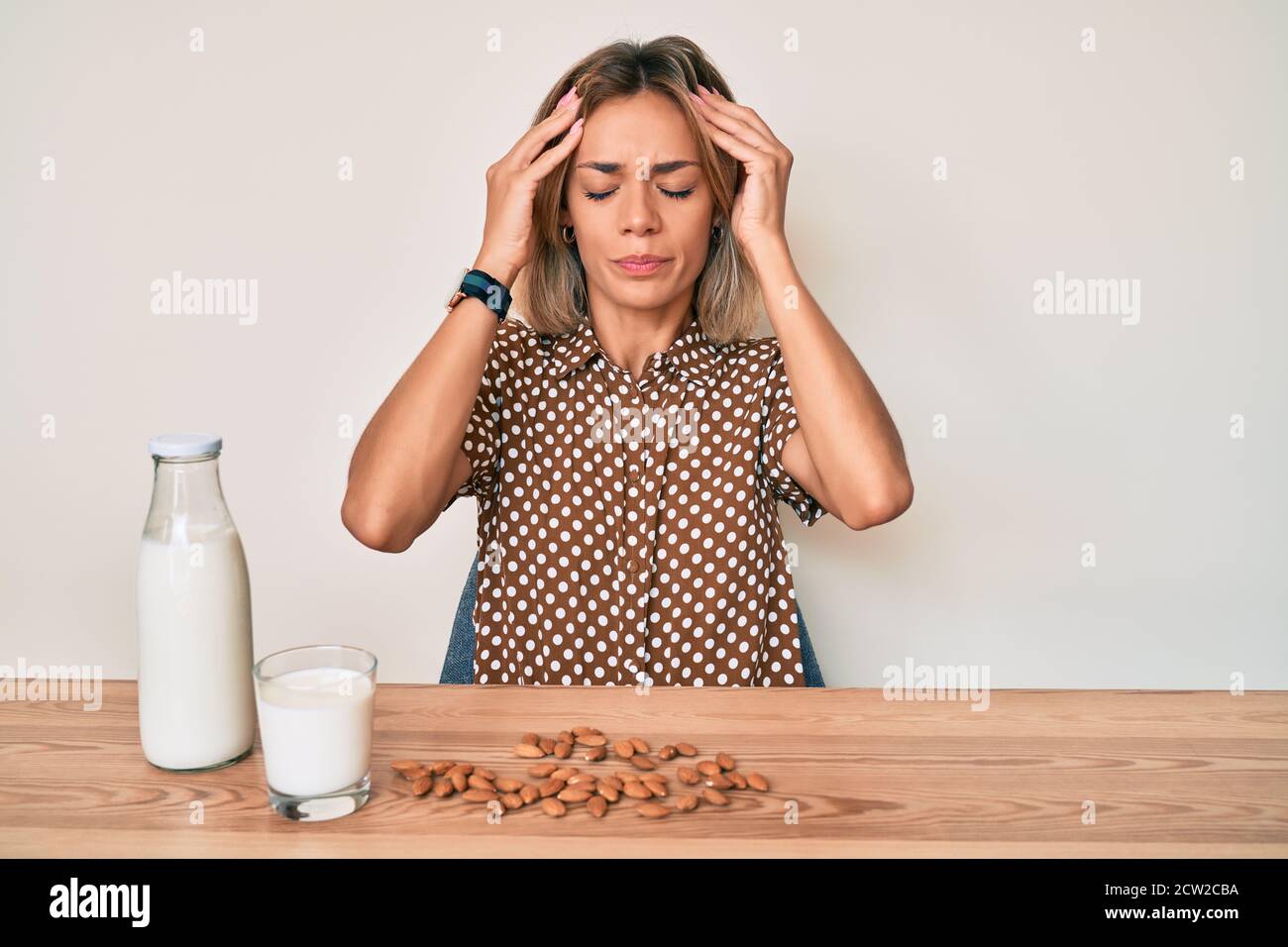 Beautiful caucasian woman drinking healthy almond milk with hand on head, headache because stress. suffering migraine. Stock Photo