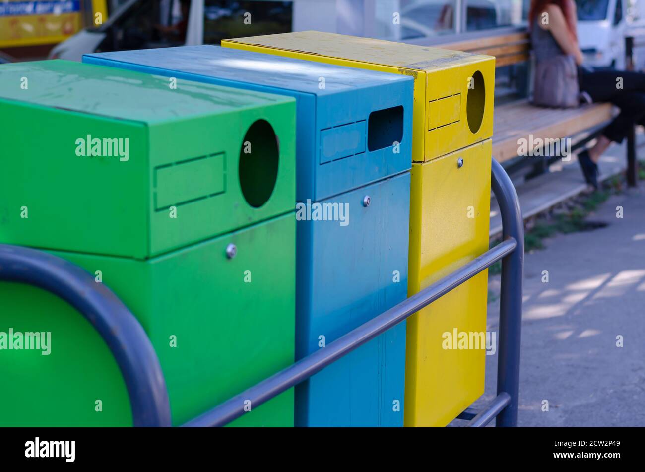 Three multicolored garbage containers on a city street. Yellow, blue