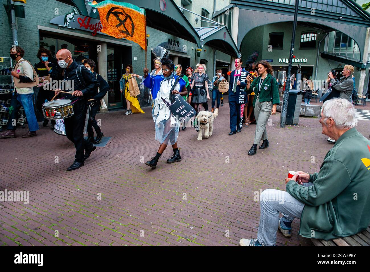 An old man sitting on a bench watching the XR (Extinction Rebellion) models passing in front of him during the demonstration.The label is made by anonymous and ego-free rebels, climate activists from Extinction Rebellion. Inclusivity and diversity are what the label stands for. The label was launched during the celebration of the Dutch Sustainable Fashion Week, and counted with around 18 creations. Through Nopulence, Extinction Rebellion expresses concern on fashion in fashion. While clothes are not for sale, they will be available for activists. Stock Photo