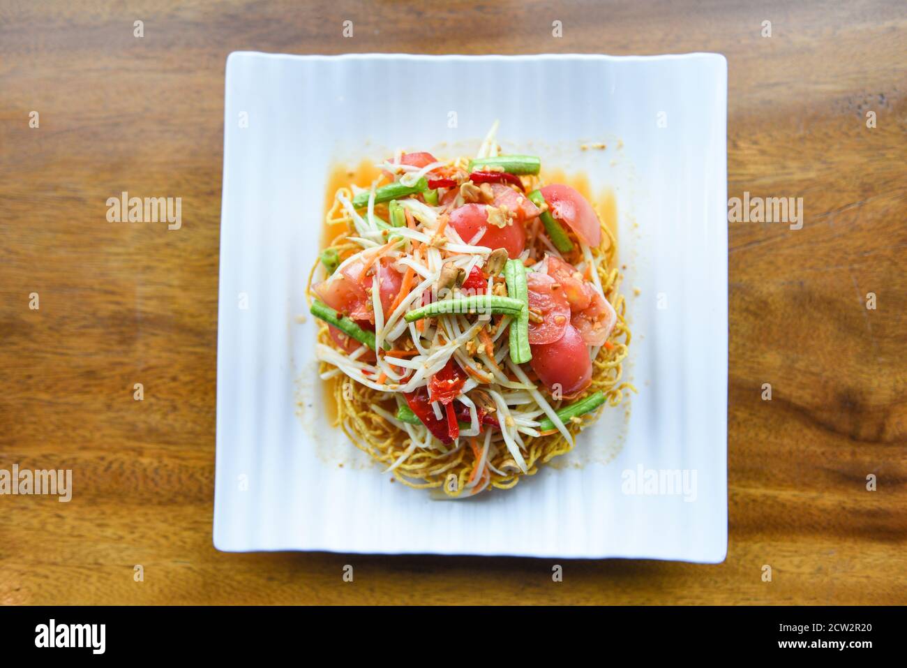 Papaya salad spicy on crispy noodles on white plate , Thai food with yardlong bean herbs and spices ingredients chilli tomato garlic Stock Photo