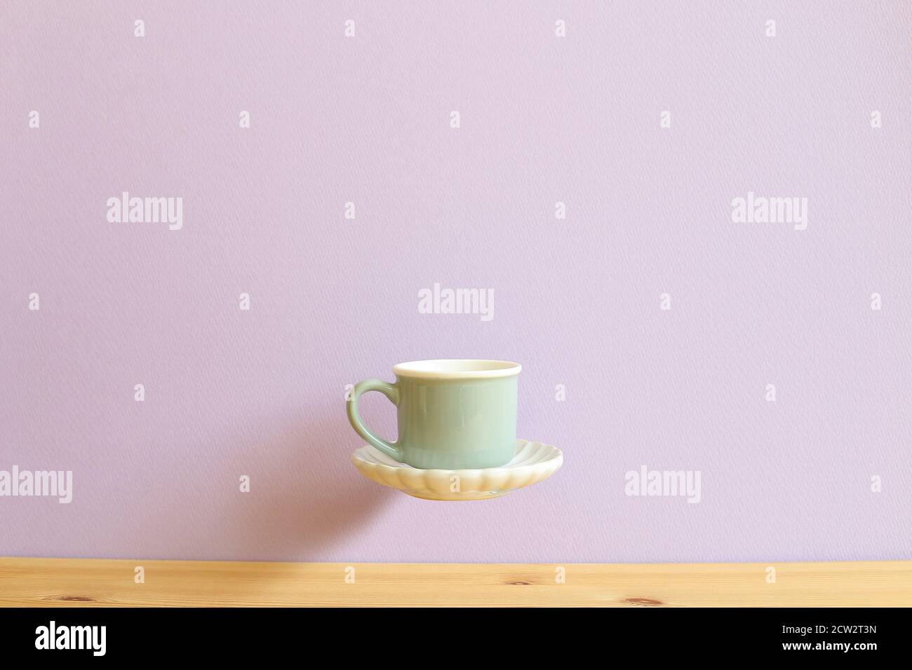 Mint green coffee cup floating on wooden table with light purple background. copy space Stock