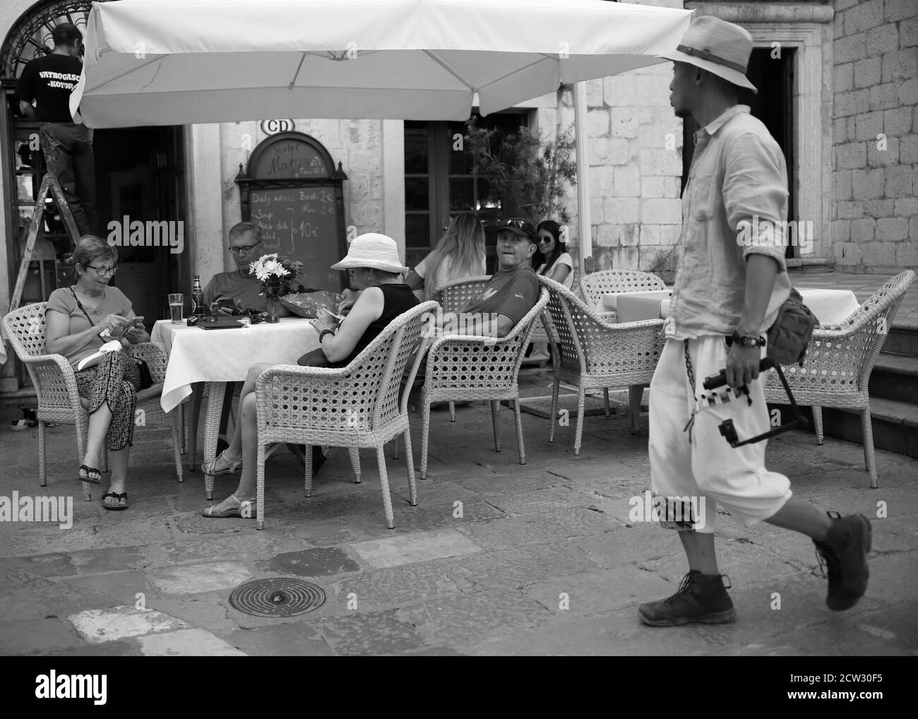 Kotor, Montenegro, Sep 22, 2019: A seated man in a cafe looking exasperated watches passer (B/W) Stock Photo