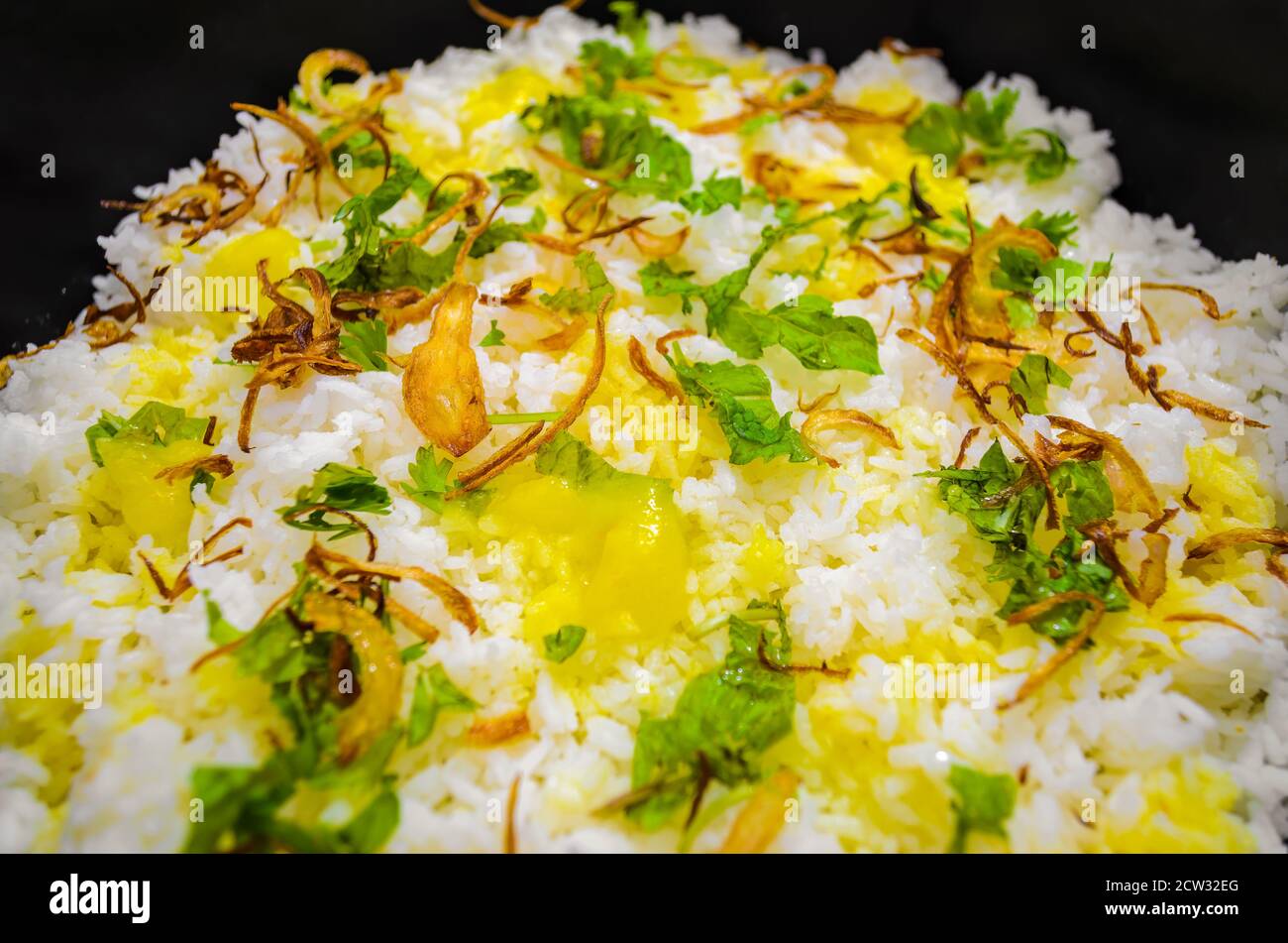 Cooked Rice in a Pan with fried onions, mint leaves, coriander leaves and ghee spread over Stock Photo