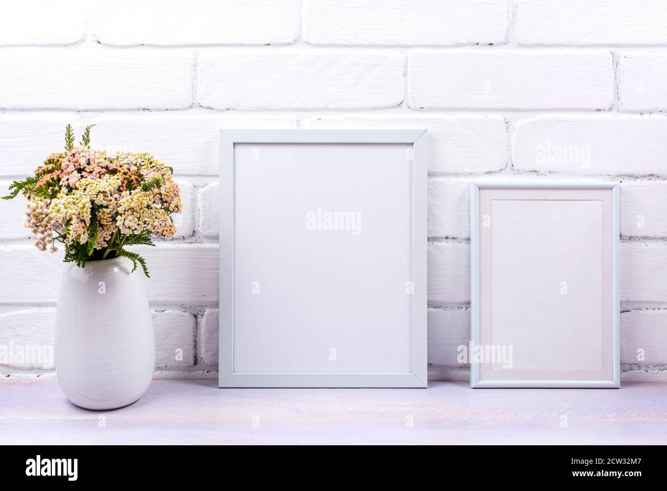 Two white frames mockup with pink yarrow wildflowers in the vase. Empty poster frame mock up for presentation design. Template framing for modern art. Stock Photo