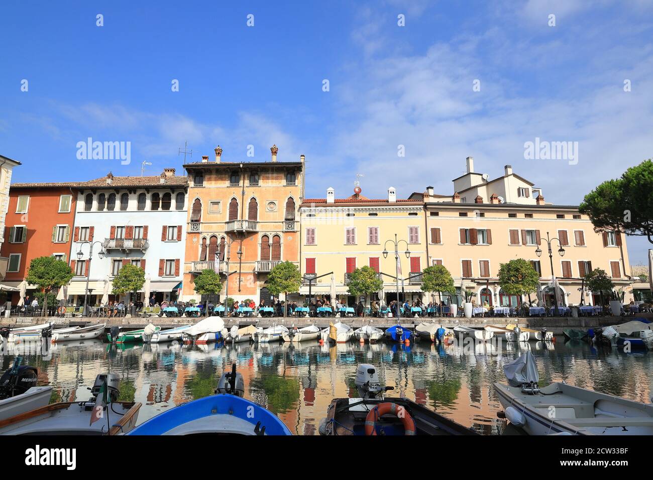 The view across boats moored in the resort town of Desenzano to cafes and restaurants.  Desenzano is on the edge of Lake Garda in North East Italy. Stock Photo