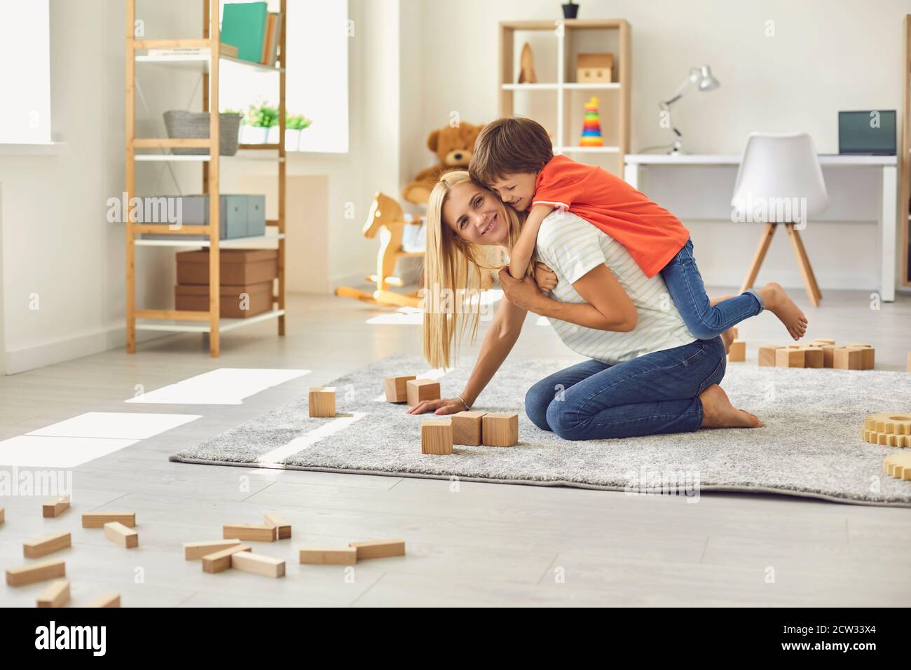 Preschool child embracing his young mommy from behind while having fun together at home Stock Photo