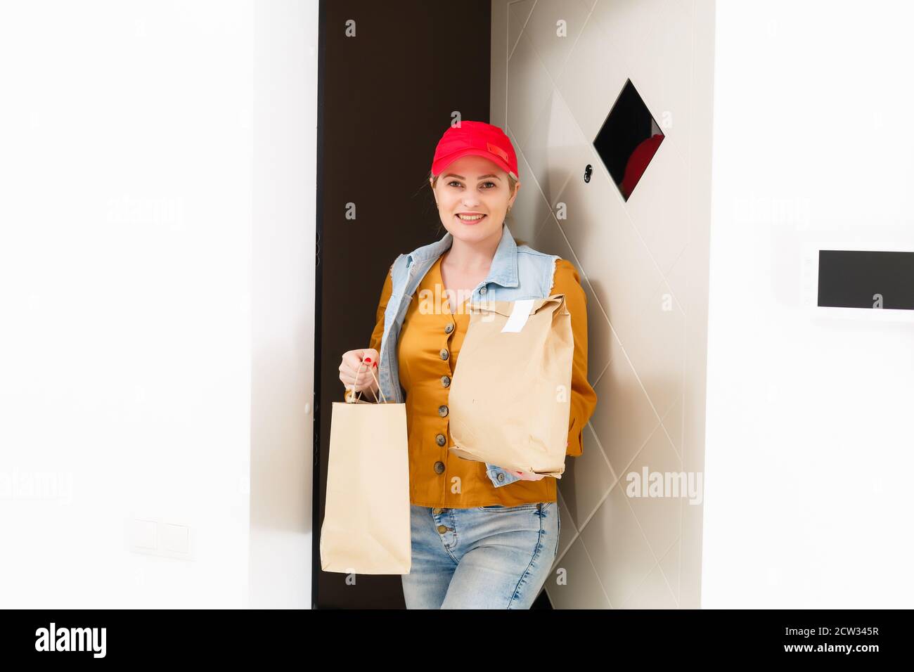 Woman in red cap giving fast food order home background. Female courier ...