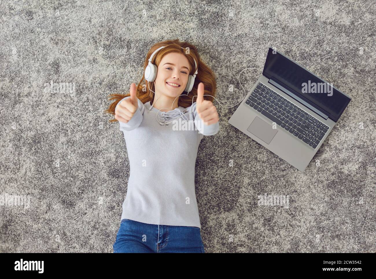 Happy young woman listening to music on gray floor Stock Photo - Alamy