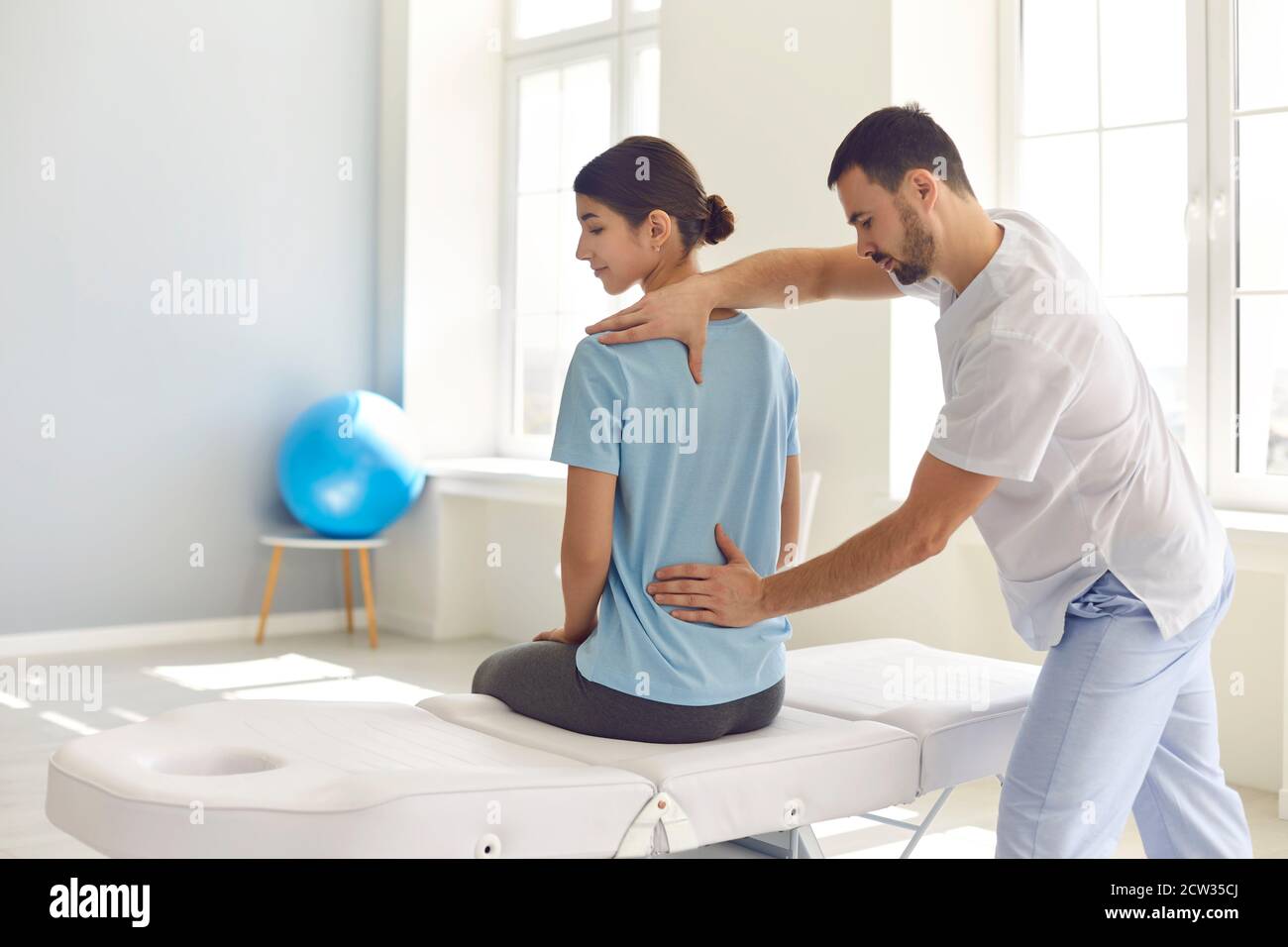 Licensed osteopath examining young female patient's back in modern hospital office Stock Photo
