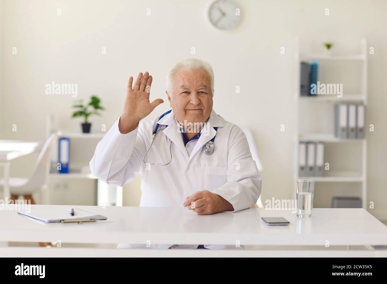 Friendly doctor waving hand welcoming clients in hospital office or on his medical video channel Stock Photo
