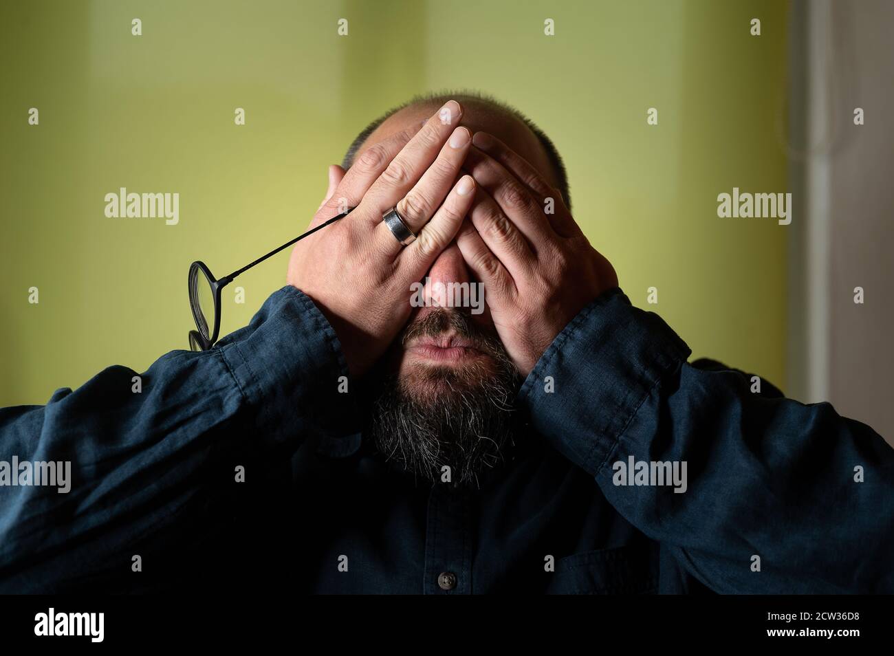 Man hides his face behind his hands so he doesn't have to see Stock Photo