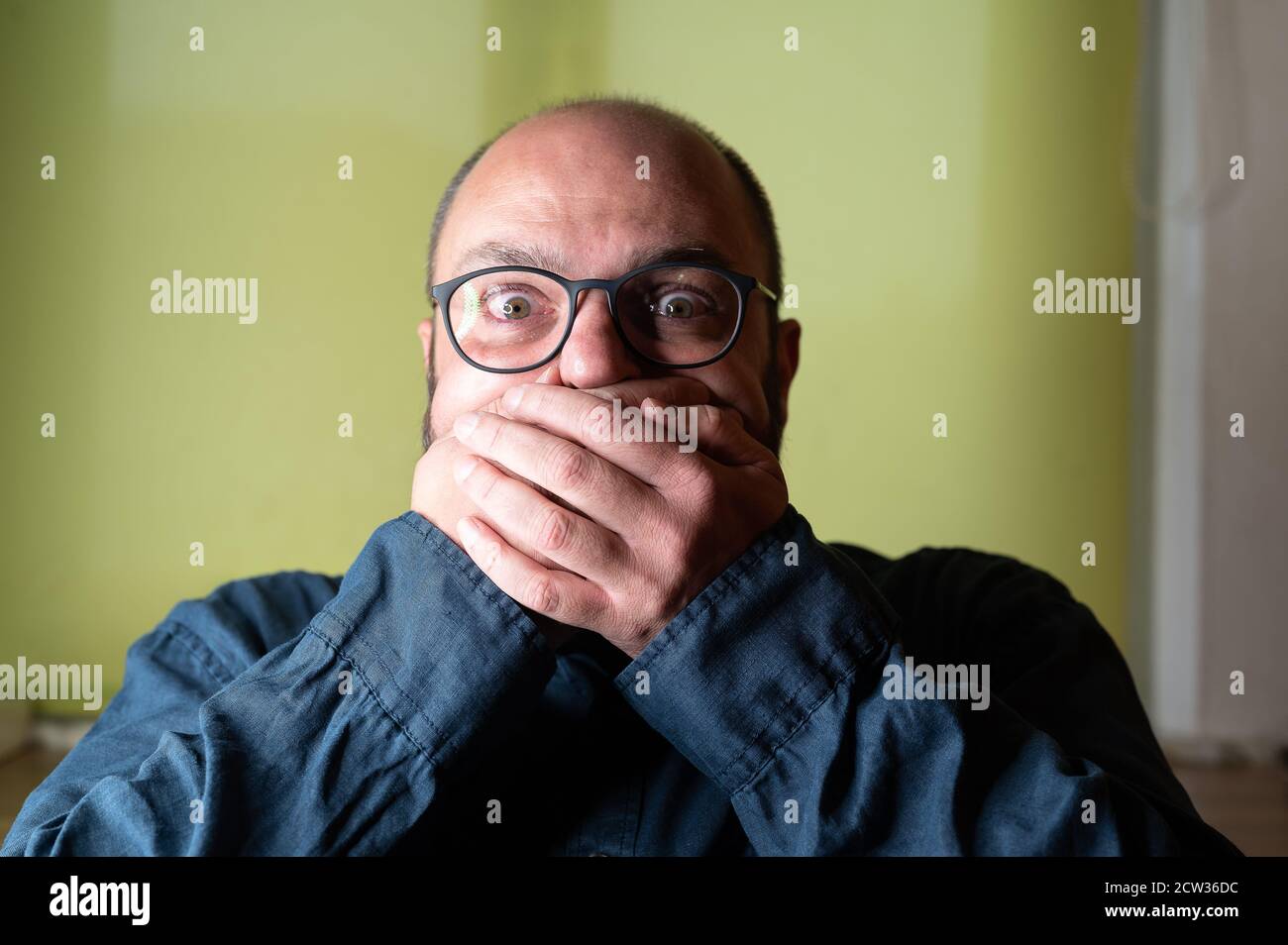 Man covers his mouth with both hands and looks scared into the camera Stock Photo