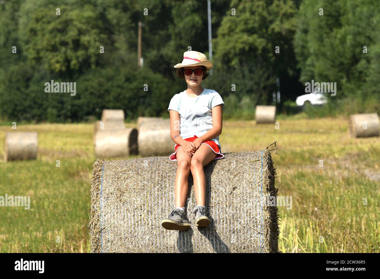 Girl sitting on a meadow after harvest on a stack of straw Stock Photo ...