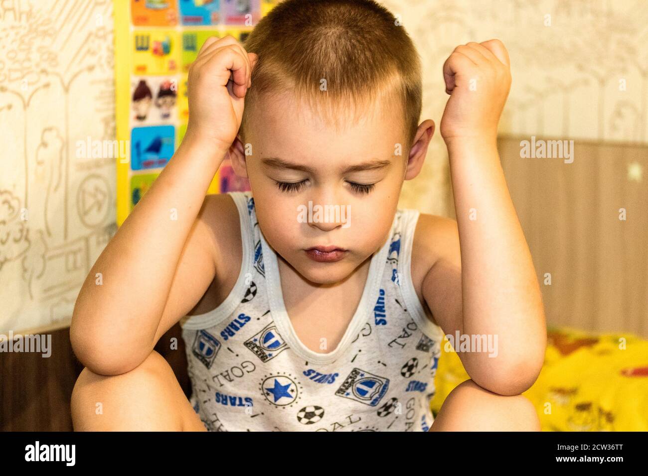 A cute little boy with his eyes closed clutched his hands by his head. Stock Photo