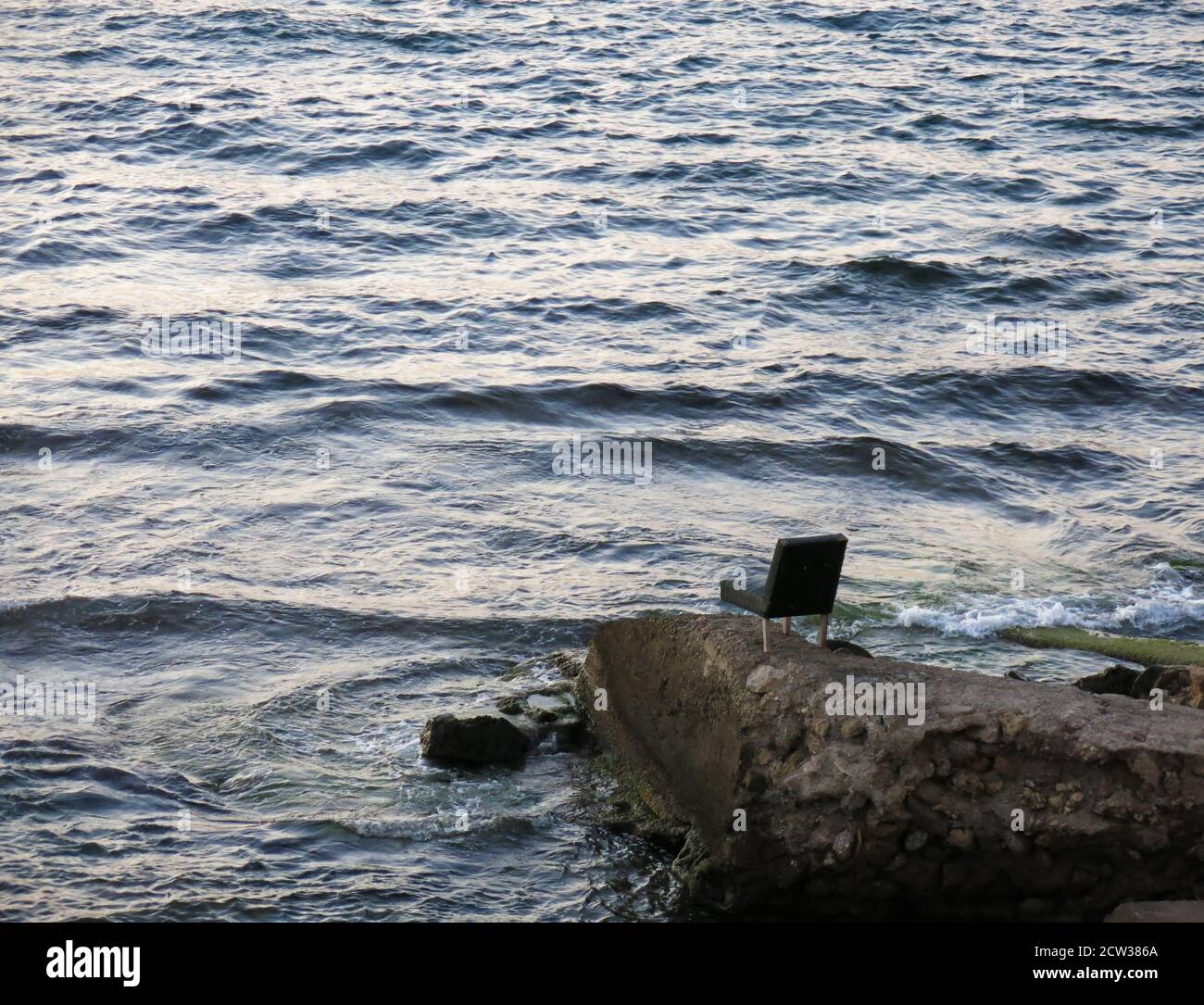 Three legged chair left on a rock by the sea. Concept: Minimalism in Photography. Stock Photo