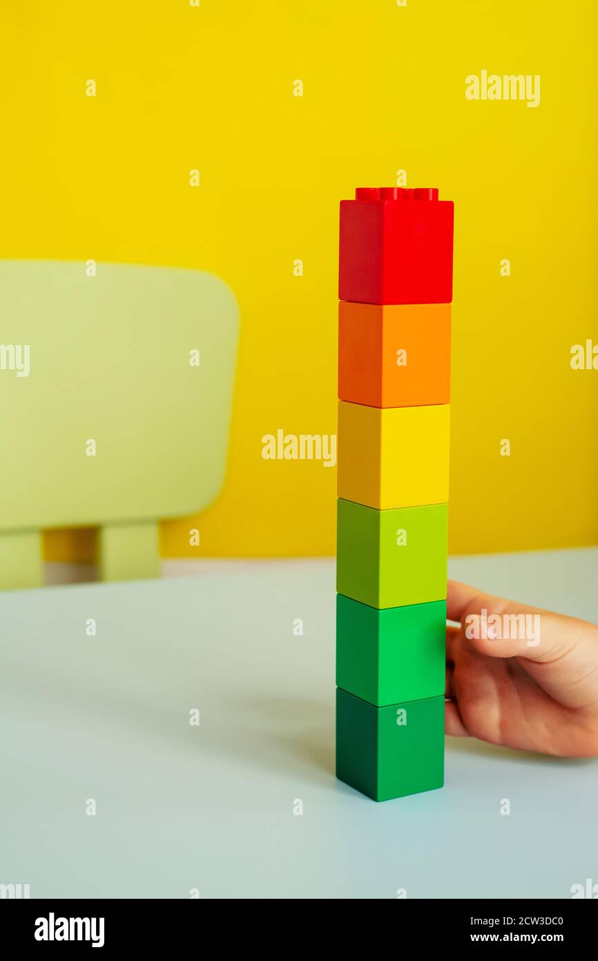 Tower of colored blocks.children's hand holding blocks.on a yellow background Stock Photo