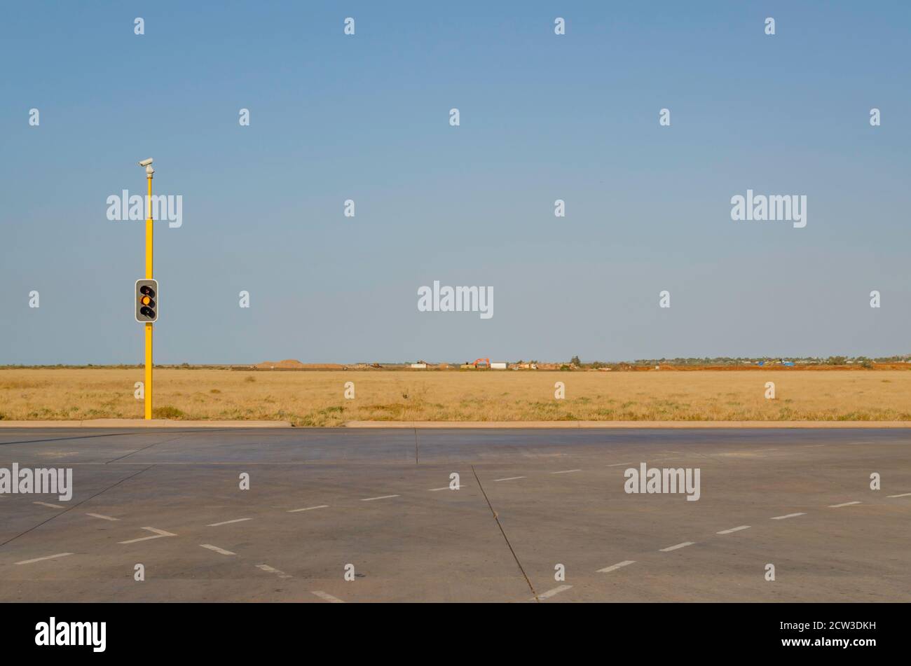 A red stop light or traffic light at a T intersection and vacant flat land in the remote mining town of Karratha, Western Australia Stock Photo