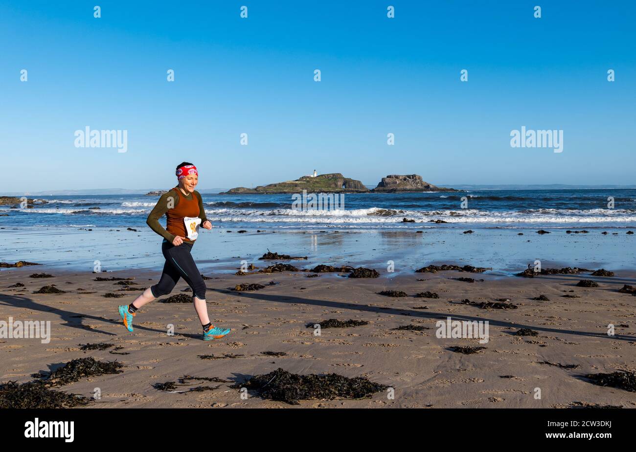 East Lothian, Scotland, United Kingdom, 27th September 2020. Scurry running event: Runners take part in a fun running event from Yellowcraig beach to North Berwick and back on a beautiful sunny Autumn morning. Fidra Island is in the background as a female runner runs on the beach Stock Photo