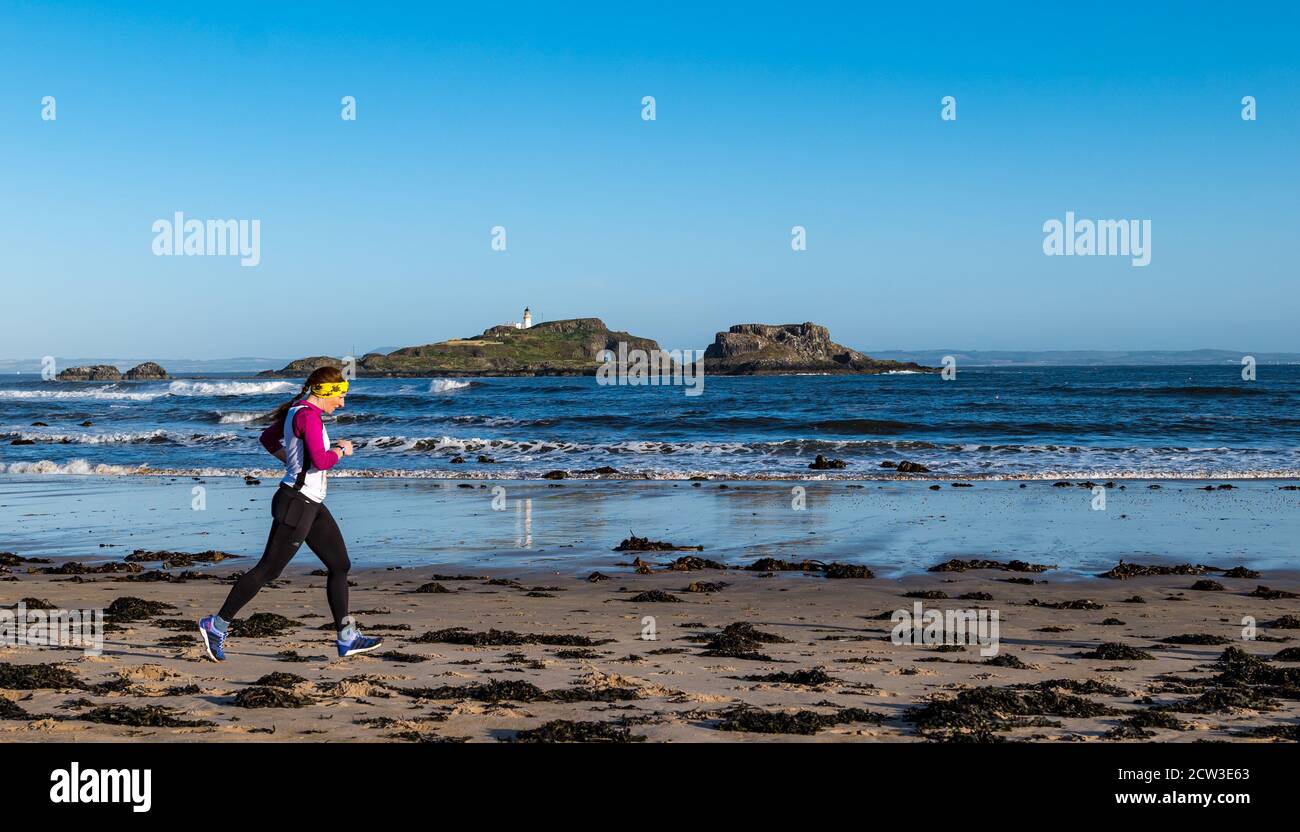 East Lothian, Scotland, United Kingdom, 27th September 2020. Scurry running event: Runners take part in a fun running event from Yellowcraig beach to North Berwick and back on a beautiful sunny Autumn morning. Fidra Island is in the background as a female runner runs on the beach Stock Photo