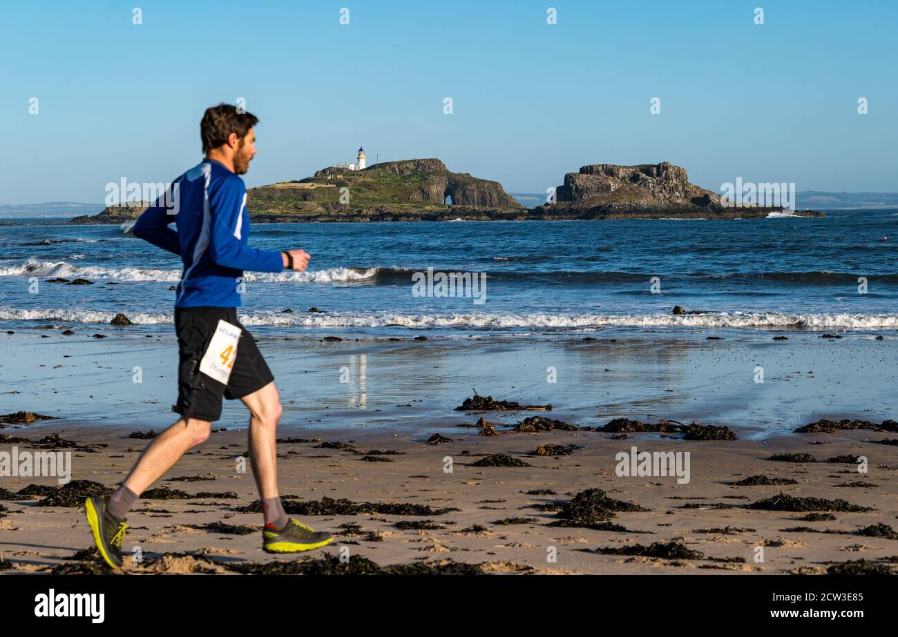 East Lothian, Scotland, United Kingdom, 27th September 2020. Scurry running event: Runners take part in a fun running event from Yellowcraig beach to North Berwick and back on a beautiful sunny Autumn morning. Fidra Island is in the background as male runner runs on the beach Stock Photo